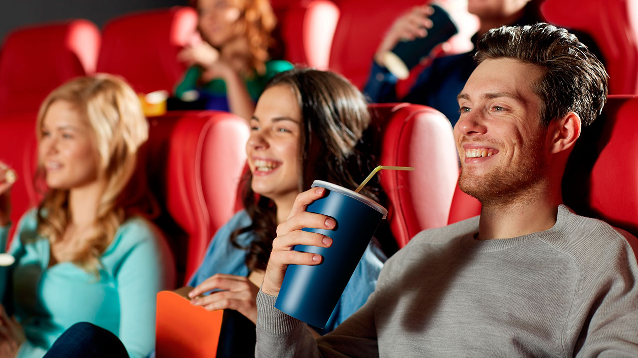 אנשים יושבים באולם קולנוע עם פופקורן וכוס שתייה